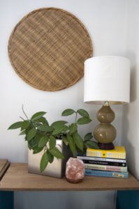 side table with plant books and lamp with wicker wall decoration